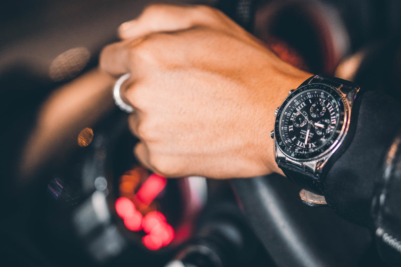 Elegant wristwatch on a hand gripping the steering wheel in a luxury car interior setting.